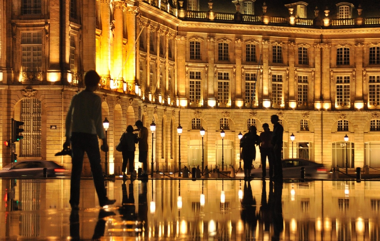 Place illuminée et reflets sur l’eau en soirée